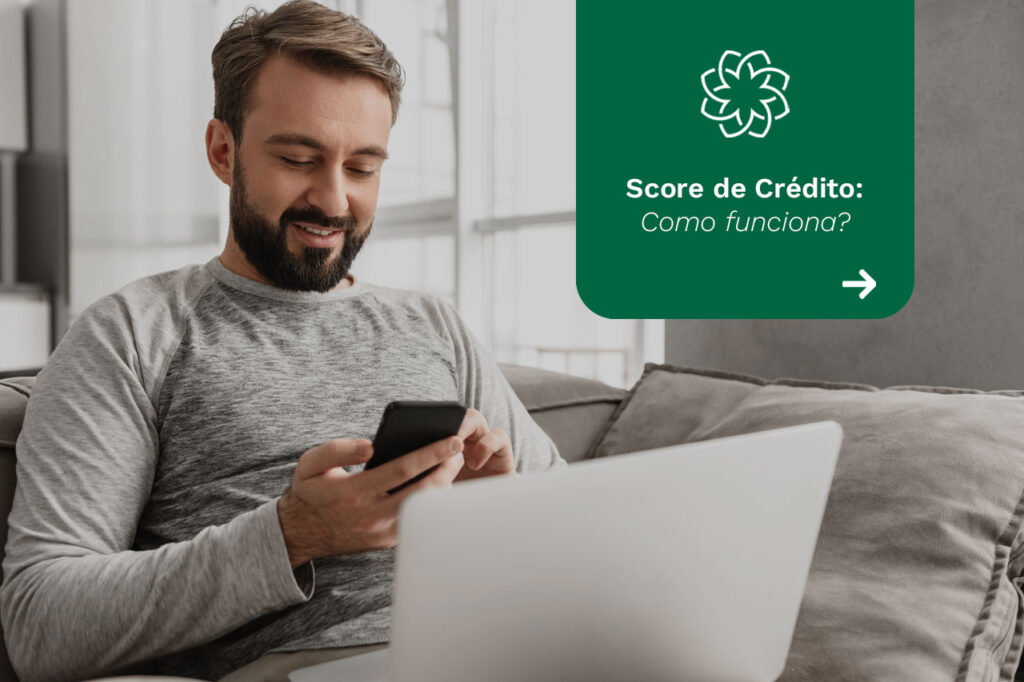 Um homem branco com o celular na mão enquanto tem o notebook no colo ao lado da frase "Score de crédito: como funciona?".